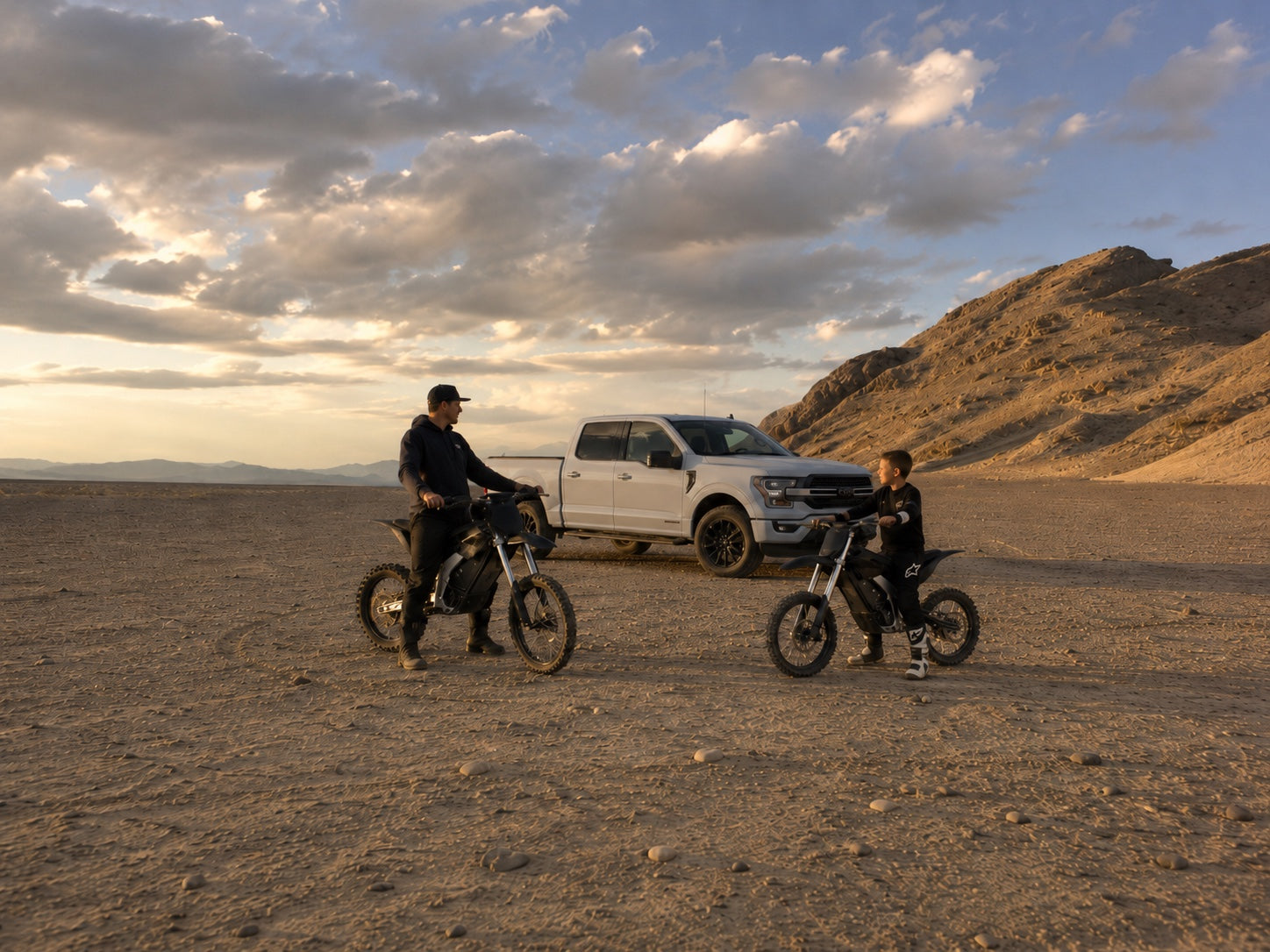 Dad and younger rider with electric dirt bikes in desert terrain